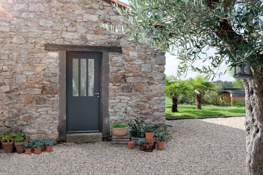 maison de campagne en pierres apparentes avec une porte d'entrée moderne style atelier en acier