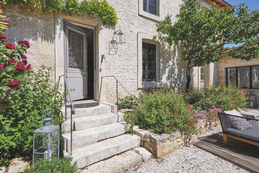 maison de campagne en pierres apparentes avec une porte d'entrée entre-ouverte avec une grille en fer forgé